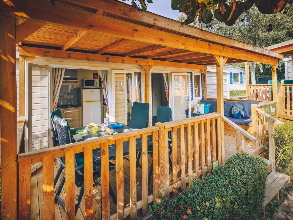 Veranda onder een houten balkenkap met een eettafel en doorkijk naar de keuken, bij een stacaravan