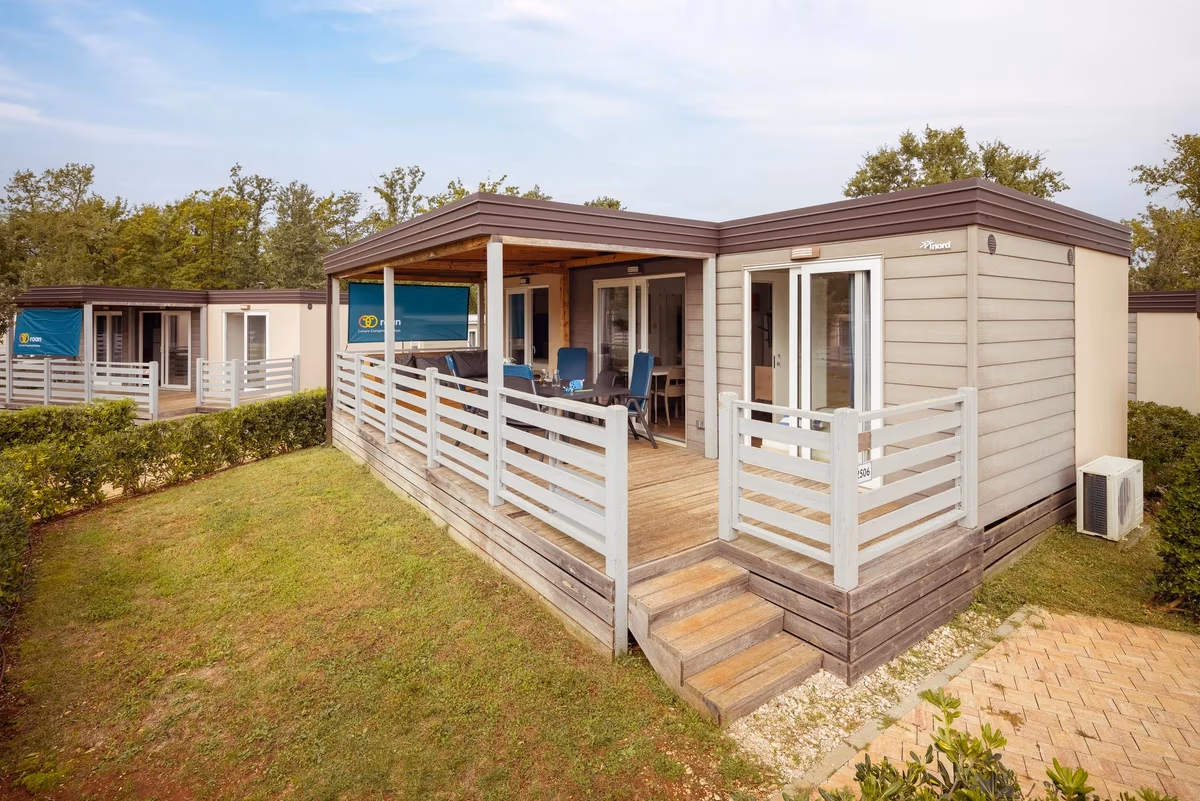 Stacaravan met een witte terrasafscheiding en houten vlonder op Camping Park Umag, met airco aan de zijkant en gras eromheen