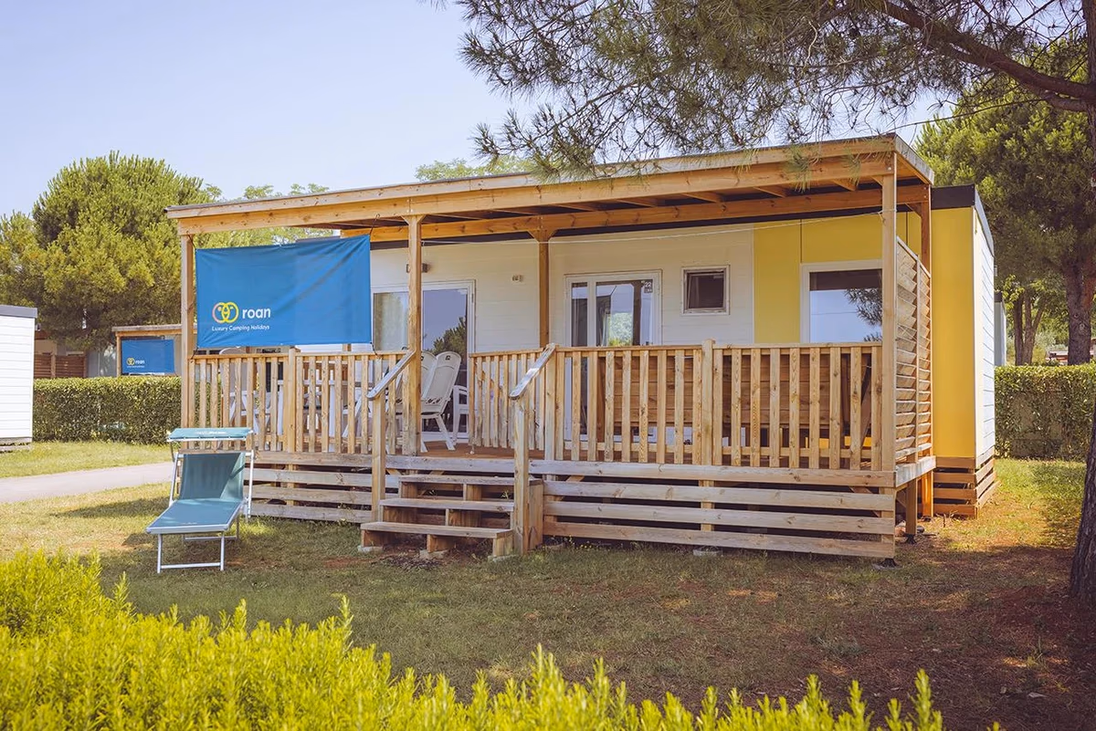 Geel-witte stacaravan met houten overkapping en veranda op Camping Park Umag, met een ligbed in het gras