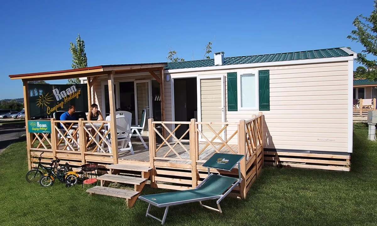 Stacaravan met groen dak en een houten terras met kruisreling op Camping Park Umag, met kinderfietsen in het gras ervoor