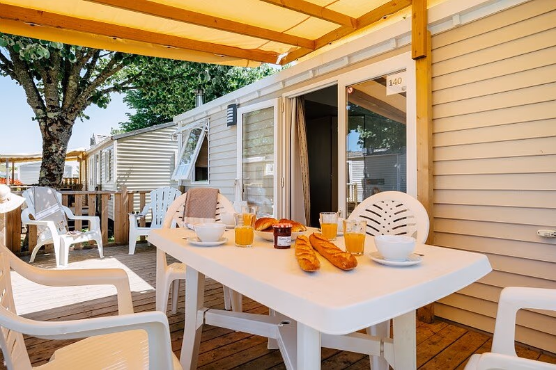 Gedekte tafel met ontbijt op het overdekte terras van een stacaravan op Camping Park Umag, onder een gele zonwering