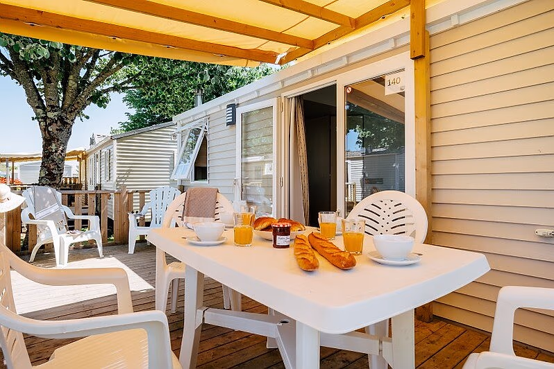 Gedekte tafel met ontbijt op het overdekte terras van een stacaravan op Camping Park Umag, onder een gele zonwering