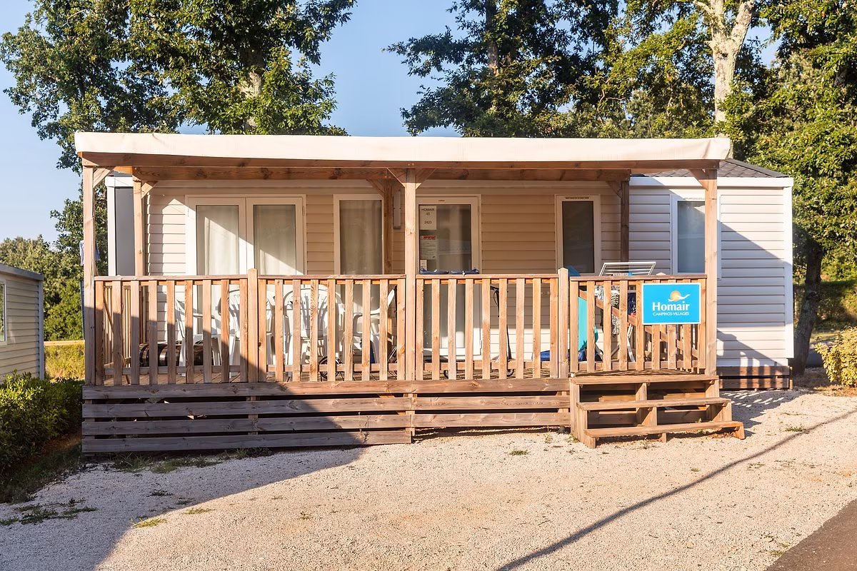 Stacaravan met een crèmekleurige luifel over de volle breedte van het terras op Camping Park Umag, aan een grindpad