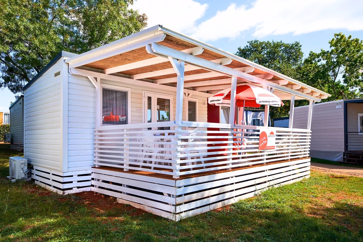 Witte stacaravan met een wit overdekt terras en een rode parasol op Camping Park Umag