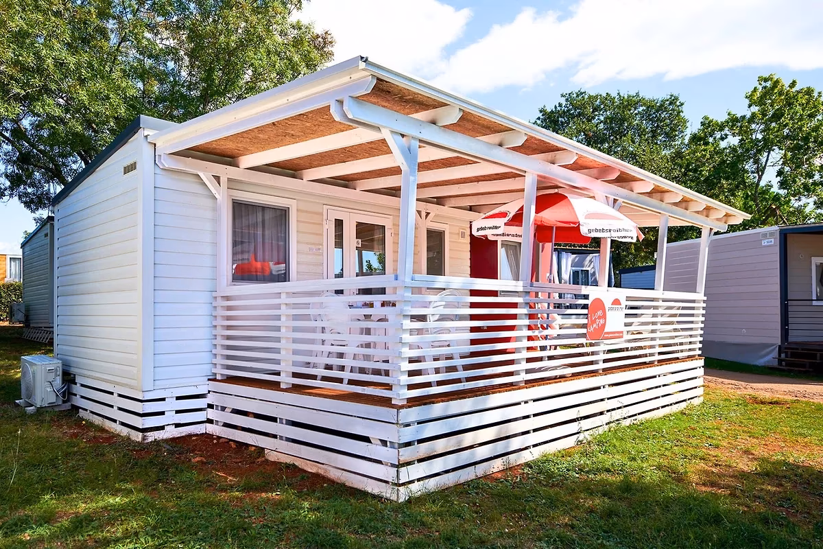 Witte stacaravan met een wit overdekt terras en een rode parasol op Camping Park Umag
