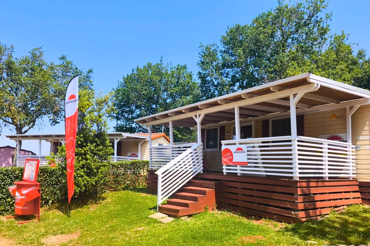 Stacaravan met een wit overdekt terras op Camping Park Umag, met reclamevlaggen van de aanbieder ernaast
