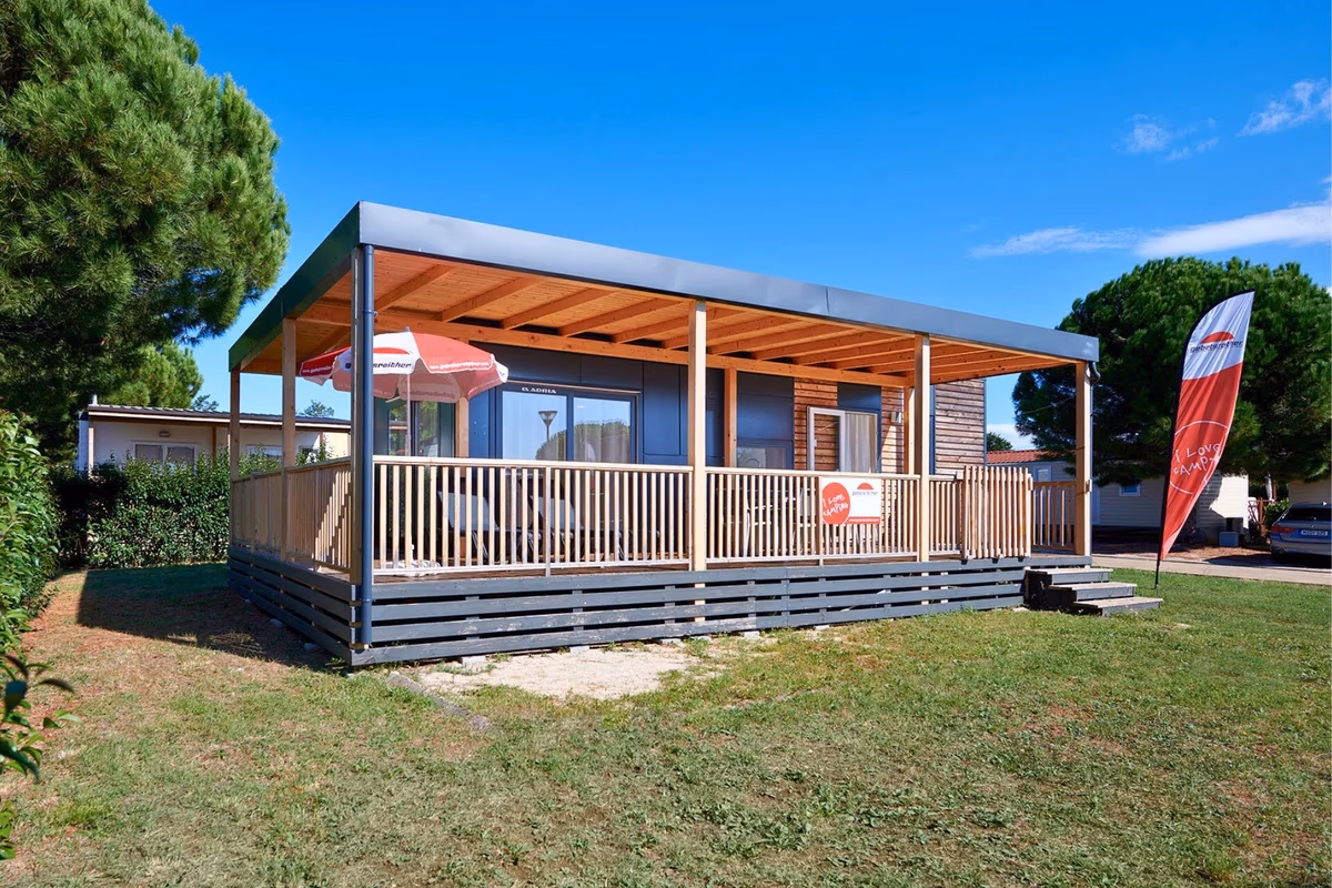 Stacaravan met een groot overdekt terras onder een stalen dak op Camping Park Umag, met een parasol en een reclamevlag ernaast