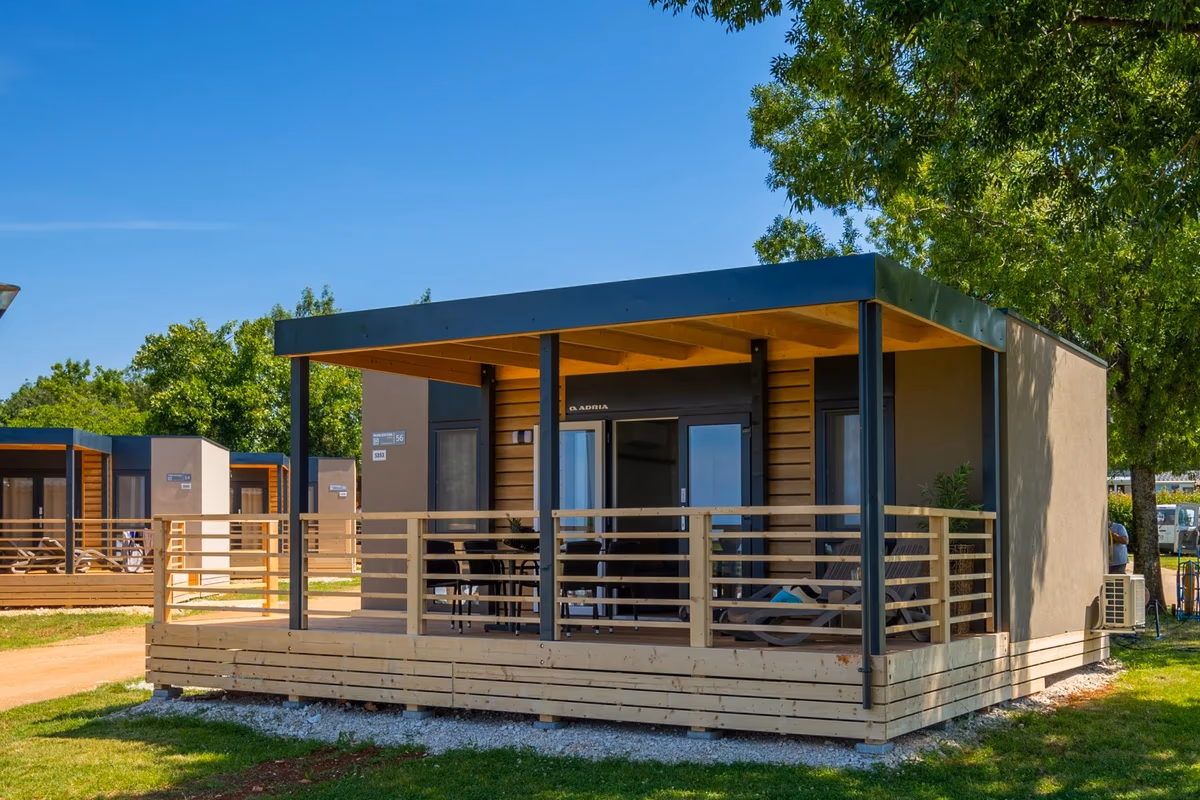 Stacaravan met houten gevel en een donker plat dak boven een ruim terras op Camping Park Umag, met een rij vergelijkbare huisjes erachter