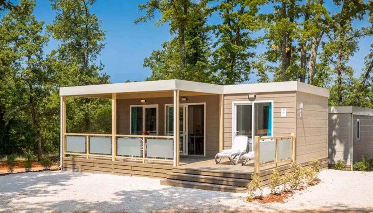 Stacaravan met plat dak en een overdekt terras met twee ligbedden op Camping Park Umag, tussen de eiken op een grindplek