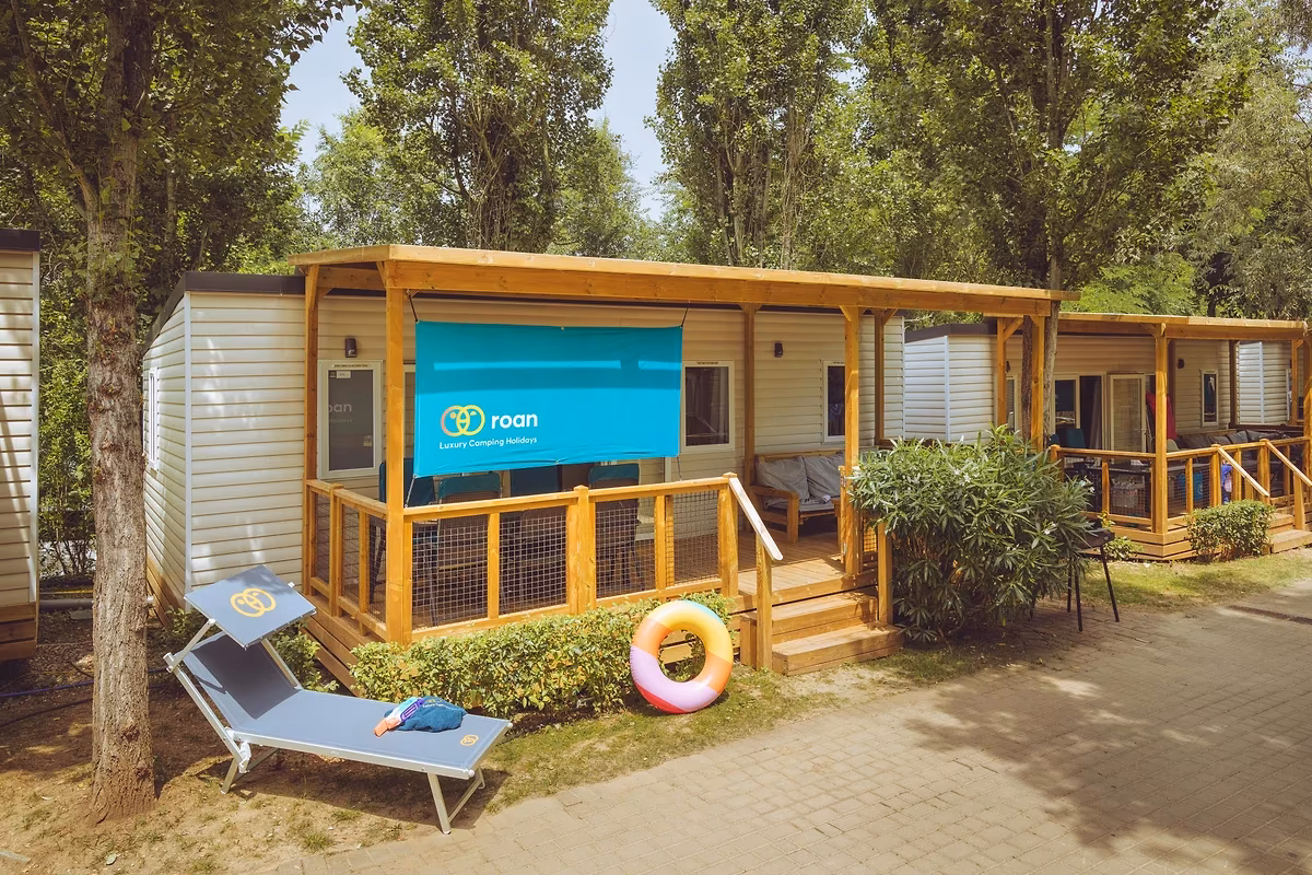 Stacaravan met een brede houten overkapping en een doek als zonwering, met een ligbed op het pad ervoor
