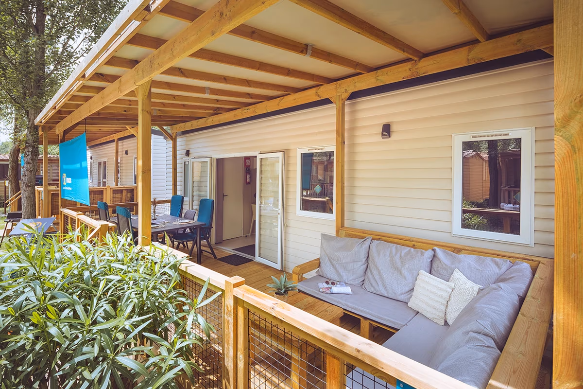 Overdekte veranda met een grijze hoekbank en een eettafel met blauwe stoelen bij een stacaravan op Camping Park Umag, met oleanders langs het terras