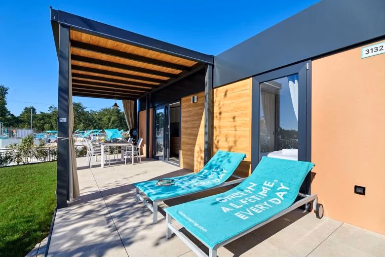 Terras met ligbedden en turquoise handdoeken bij een stacaravan aan het zwembad van Camping Park Umag