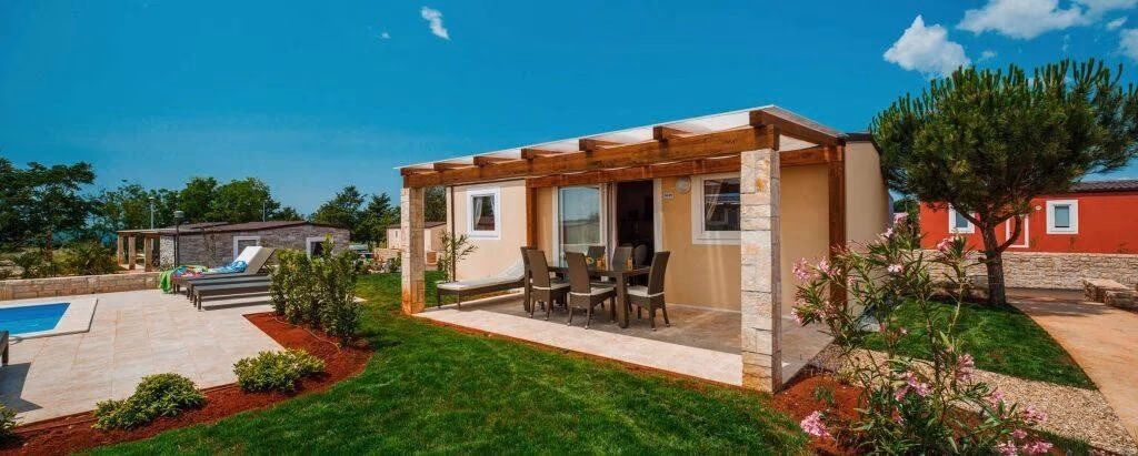 Accommodatie met natuurstenen gevel en een overdekt terras met eettafel op Camping Park Umag, met een zwembad in de tuin ernaast