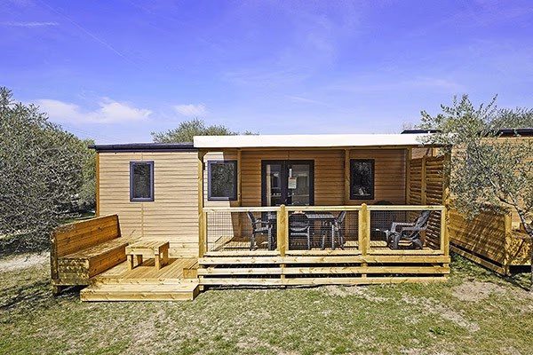 Stacaravan met houten gevel, een overdekt terras en een houten bank ernaast op Camping Park Umag