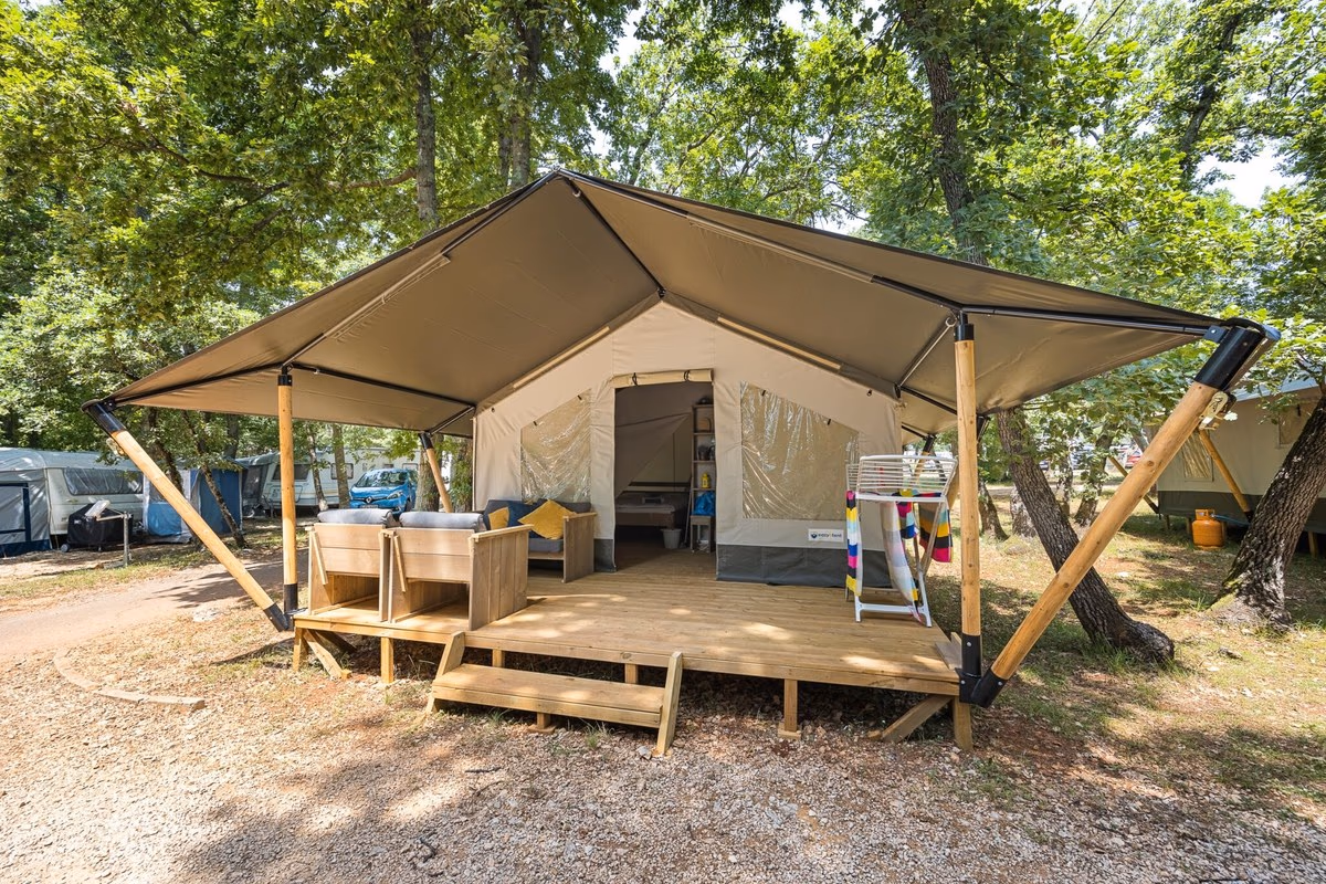 Safaritent met een brede luifel op houten schoren en loungebankjes op het terras, tussen de eiken op Camping Park Umag