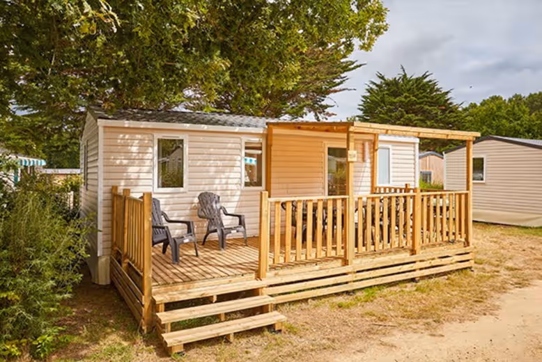 Stacaravan met een houten terras en twee stoelen onder de bomen op Camping Park Umag