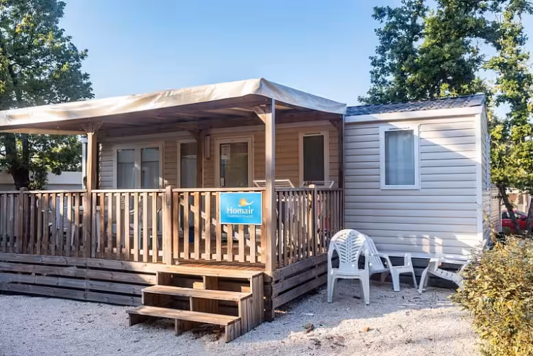Stacaravan met een lichte luifel boven het houten terras op Camping Park Umag, met witte tuinstoelen op het grind