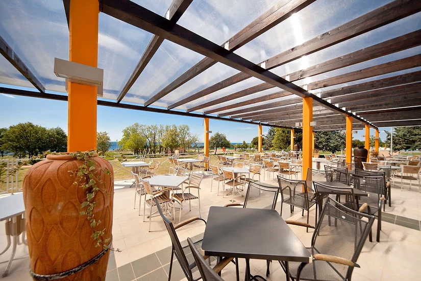 Restaurantterras onder een glazen pergola met oranje palen en zicht op zee op Camping Park Umag