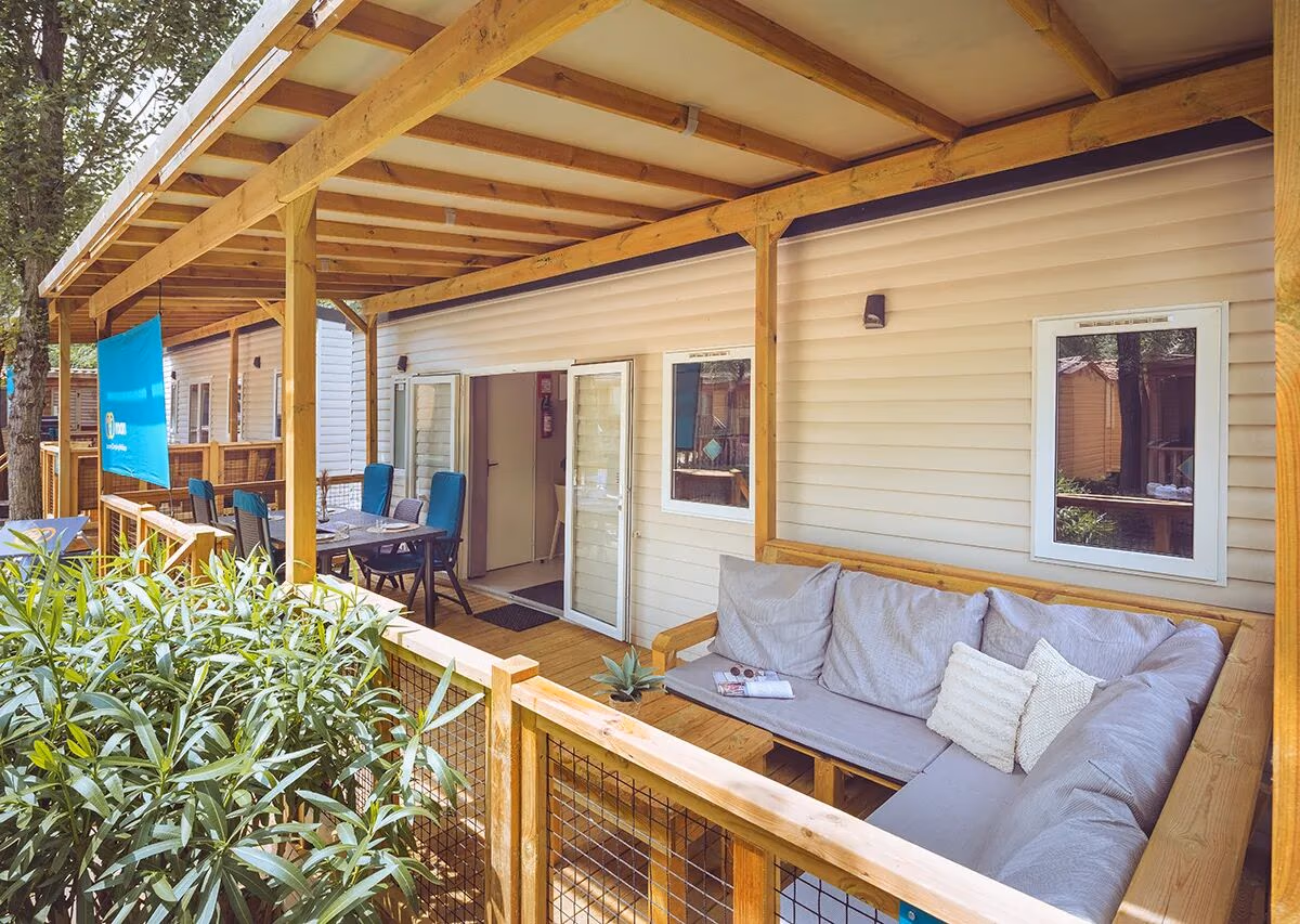 Overdekte veranda met een grijze hoekbank en een eettafel met blauwe stoelen bij een stacaravan op Camping Park Umag