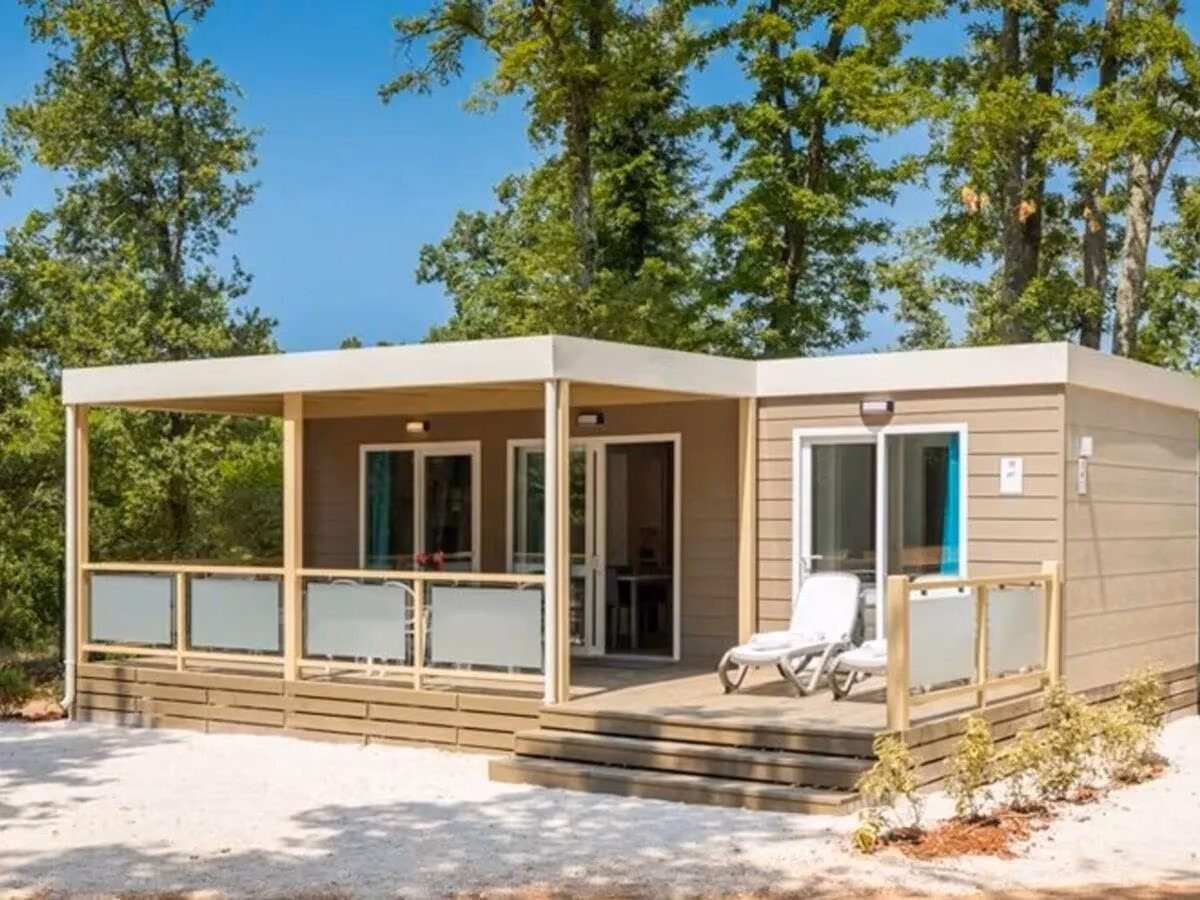 Stacaravan met plat dak en een overdekt terras met twee ligbedden op Camping Park Umag, op een grindplek tussen de eiken