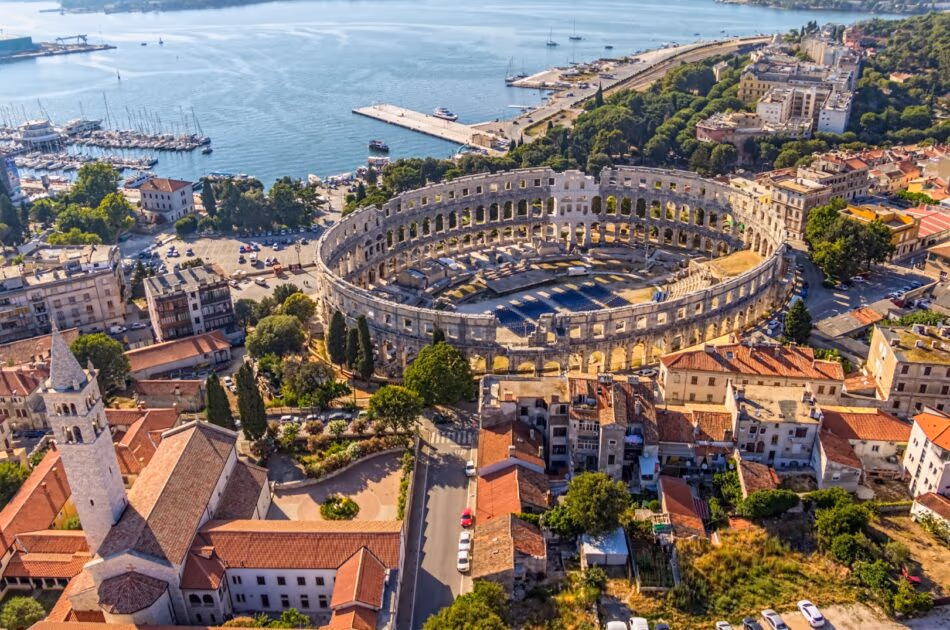 De ovale Arena van Pula tussen de rode daken, met boten in de haven op de achtergrond